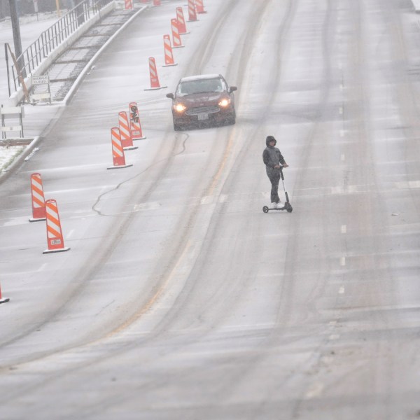 Snow falls as a car and a scooter make their way along a street Thursday, Jan. 9, 2025, in Dallas. (AP Photo/LM Otero)