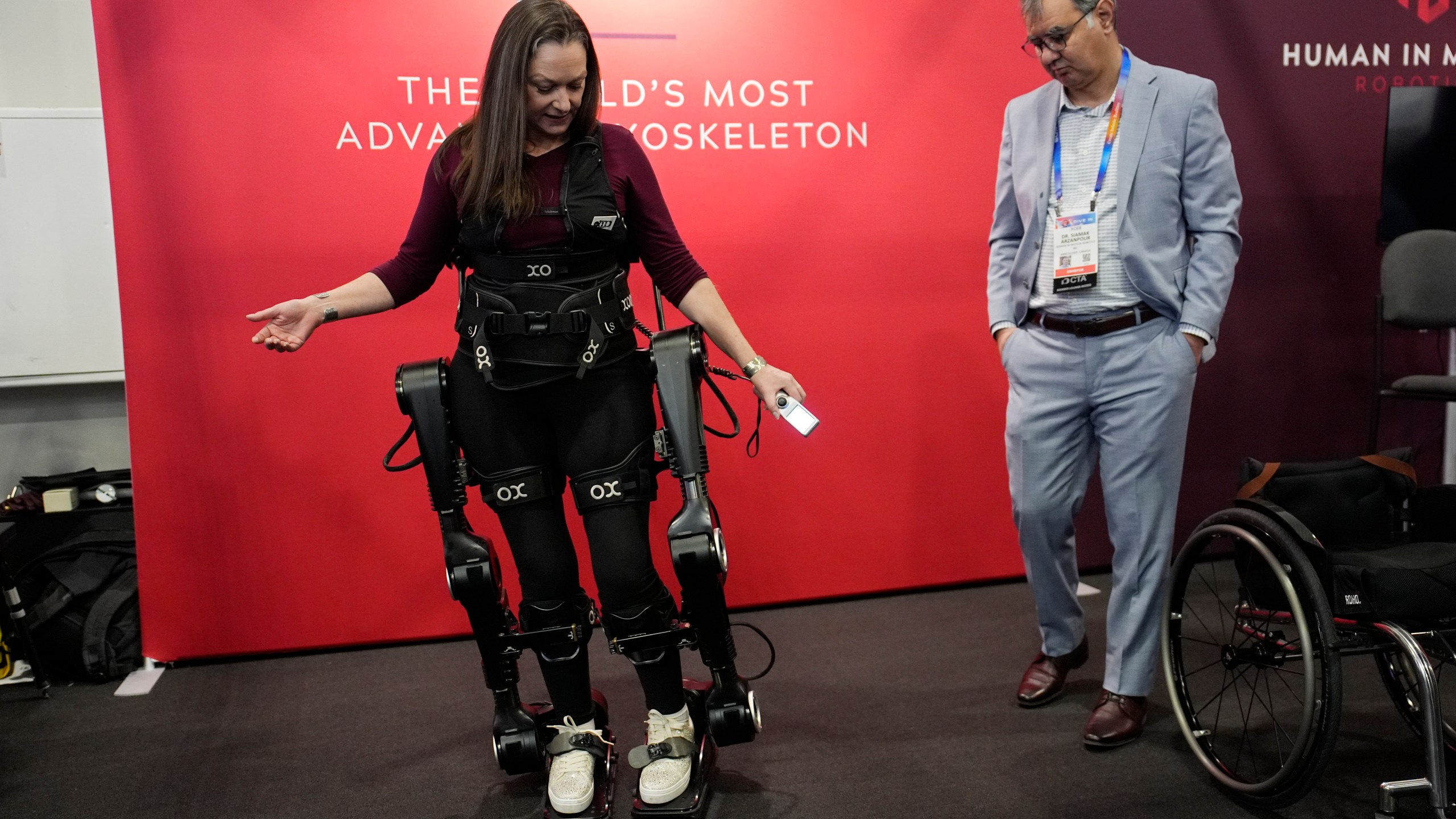 Chloe Angus, director of Lived Experience at Human in Motion Robotics and paraplegic, stands and moves with help from the XoMotion exoskeleton at the Human In Motion Robotics booth during the CES tech show Wednesday, Jan. 8, 2025, in Las Vegas. The wearable robotic exoskeleton is designed to assist patients with mobility impairments due to spinal cord injuries, stroke and other neurological conditions in standing up and walking. (AP Photo/John Locher)