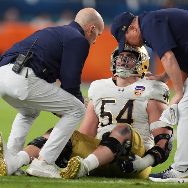 Notre Dame offensive lineman Anthonie Knapp (54) is assisted on the field during the first half of the Orange Bowl NCAA College Football Playoff semifinal game against Penn State, Thursday, Jan. 9, 2025, in Miami Gardens, Fla. (AP Photo/Rebecca Blackwell)