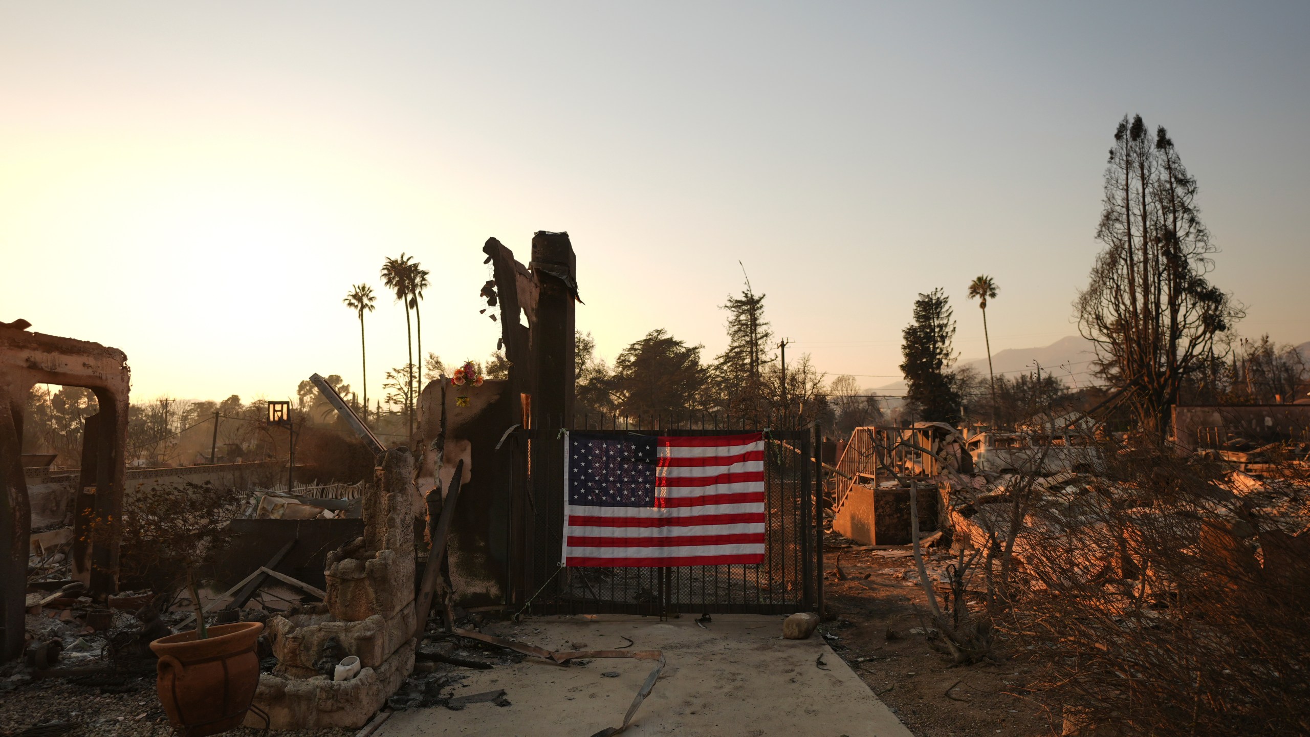 An American flag hangs on the gate of a home destroyed by the Eaton Fire in Altadena, Calif., Friday, Jan. 10, 2025. (AP Photo/Jae C. Hong)