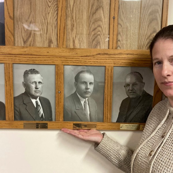 In this photo provided by Dan Donaldson, Dana Klabenes, the city clerk in Neligh, Neb., holds her hand under a photo of former Mayor Fred Benning, a World War I veteran who is being honored by having an Army base in Georgia renamed Fort Benning in his honor, at city hall on Tuesday, March 4, 2025. (Dan Donaldson via AP)