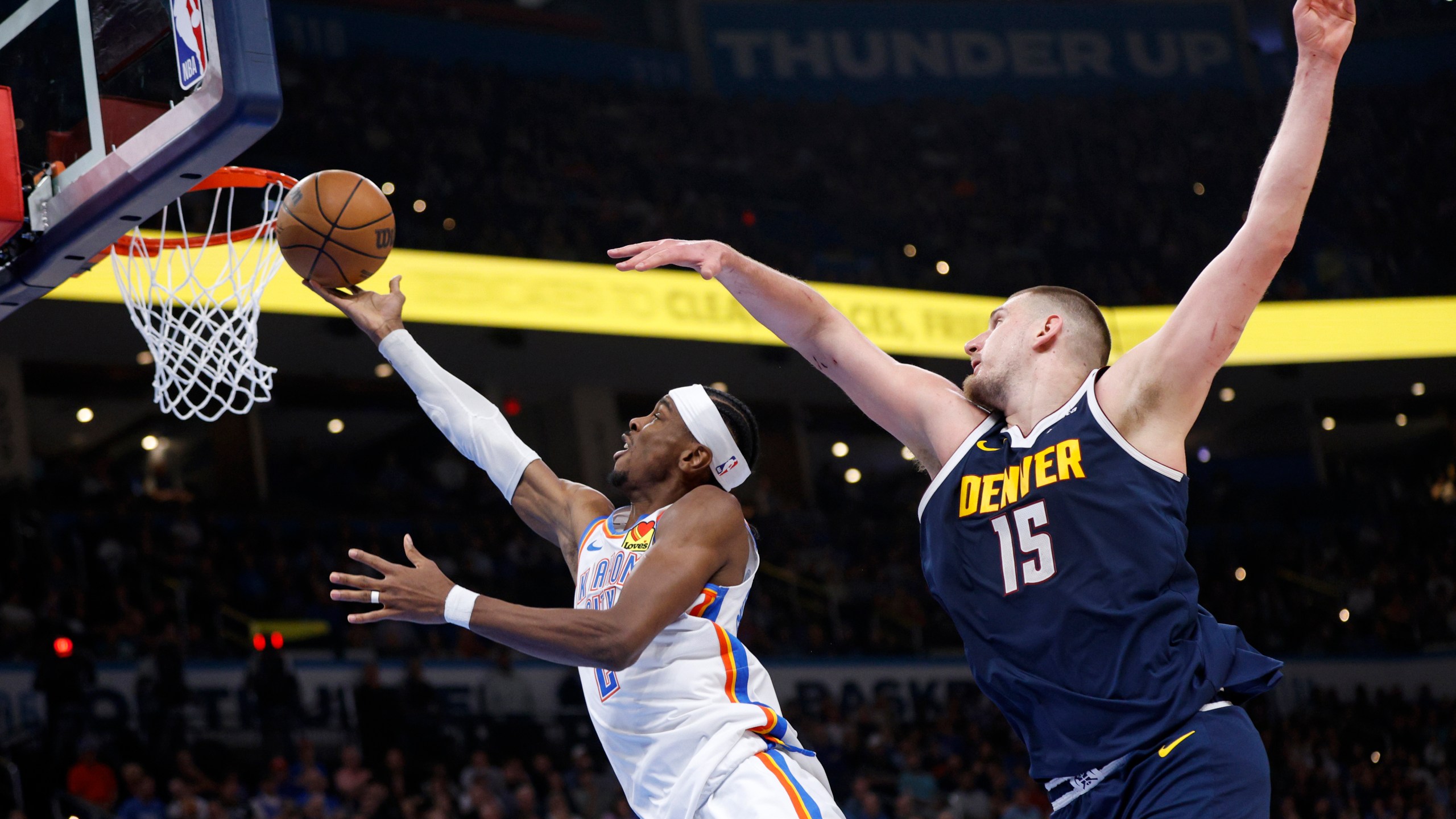 Oklahoma City Thunder guard Shai Gilgeous-Alexander, left, takes the ball to the basket in front of Denver Nuggets center Nikola Jokic (15) during the first half of an NBA basketball game Monday, March 10, 2025, in Oklahoma City. (AP Photo/Nate Billings)