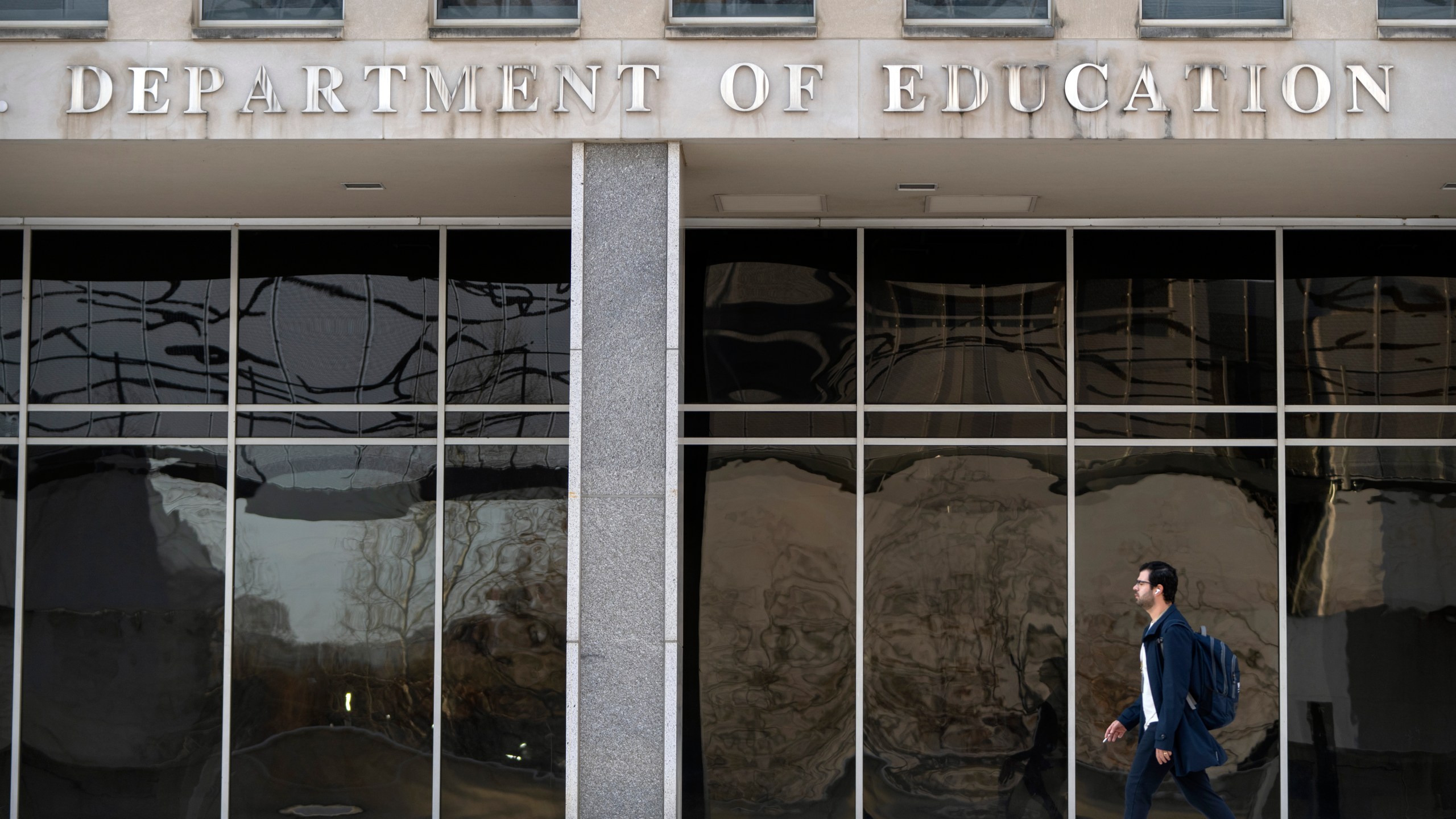 A commuter walks past the headquarters of the U.S. Department of Eduction, which were ordered closed for the day for what officials described as security reasons amid large-scale layoffs, Wednesday, March 12, 2025, in Washington. (AP Photo/Mark Schiefelbein)